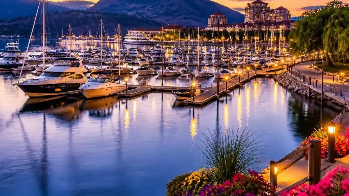A lit marina and downtown waterfront at dusk with flower beds in the foreground
